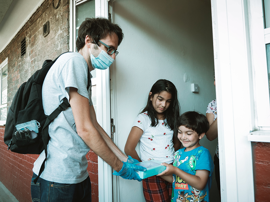 man in mask giving package to children