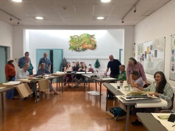 Photo shows a group of people in a large room. Each person is painting a picture. 