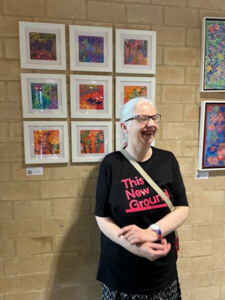 Tara, a This New Ground artist, standing in front of some of her paintings