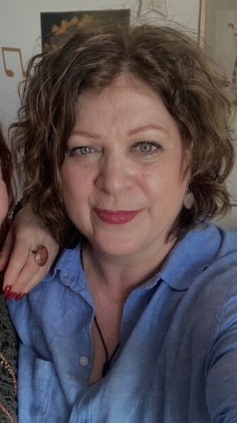 Angie, a white woman in her early 60s with brown curly hair and a big smile.