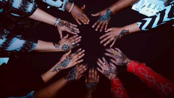 Women's hands facing inwards to create a circle of solidarity. The hands are a range of colours and have beautiful henna patterns on.