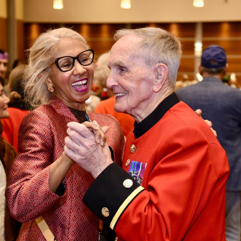 Two people dancing. One is a woman. The other is an older man, dressed in a red service uniform and wearing medals.
