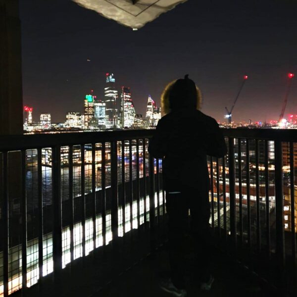 A teenager with his back to the camera, looking out over the Thames at the city lights