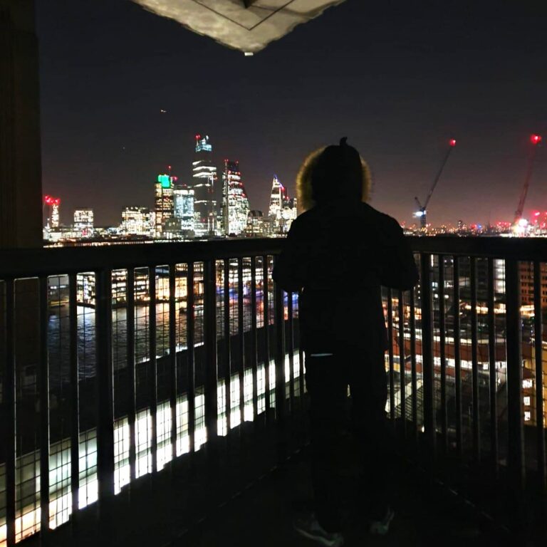 A teenager with his back to the camera, looking out over the Thames at the city lights