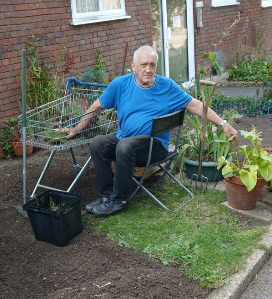 Ken, a man in his 60s, gardening from a chair.
