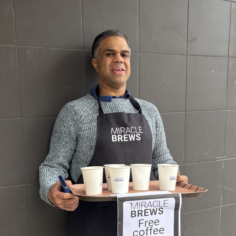 A man wearing a a Petit Miracles apron, serving coffee