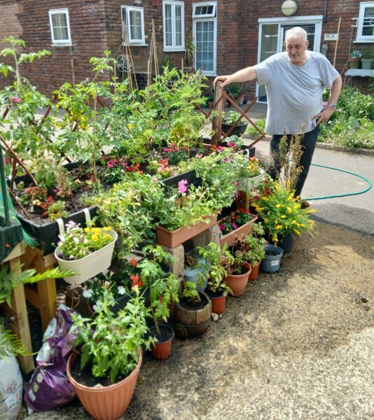 Ken, a man in his 60s, standing by a trug full of plants and surrounded by pots of plants