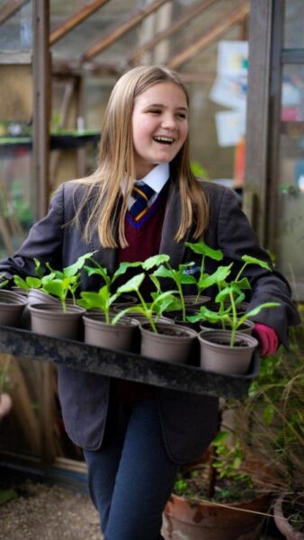 A smiling girl carrying a tray of plants.