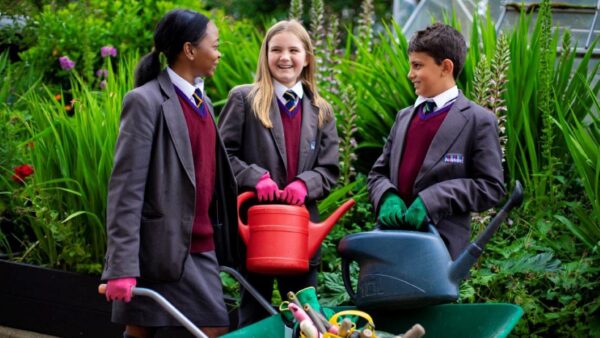 Two girls and a boy holding watering cans. They're all smiling and wearing school uniform.