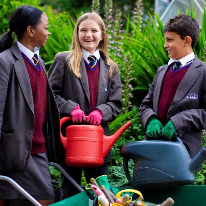 Two girls and a boy holding watering cans. They're all smiling and wearing school uniform.