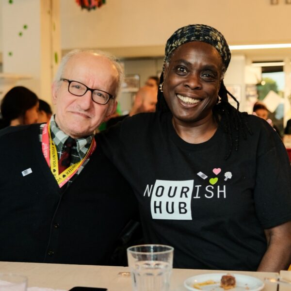 A man and a woman smiling at the camera. She is wearing a Nourish Hub T-shirt so is likely a volunteer